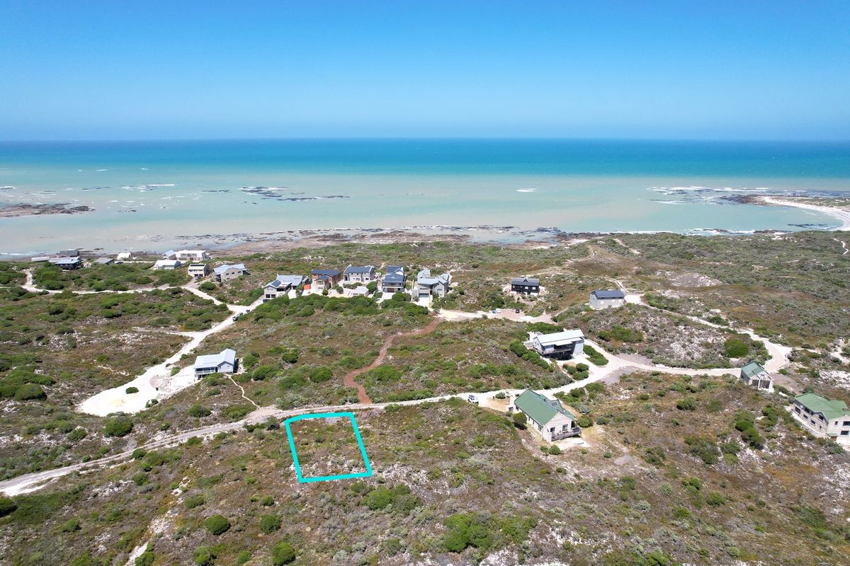 Aerial view of a vacant residential plot situated in a coastal estate, offering proximity to the ocean and surrounding natural landscape.