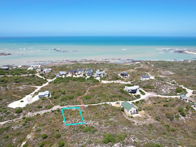 Aerial view of a vacant residential plot situated in a coastal estate, offering proximity to the ocean and surrounding natural landscape.