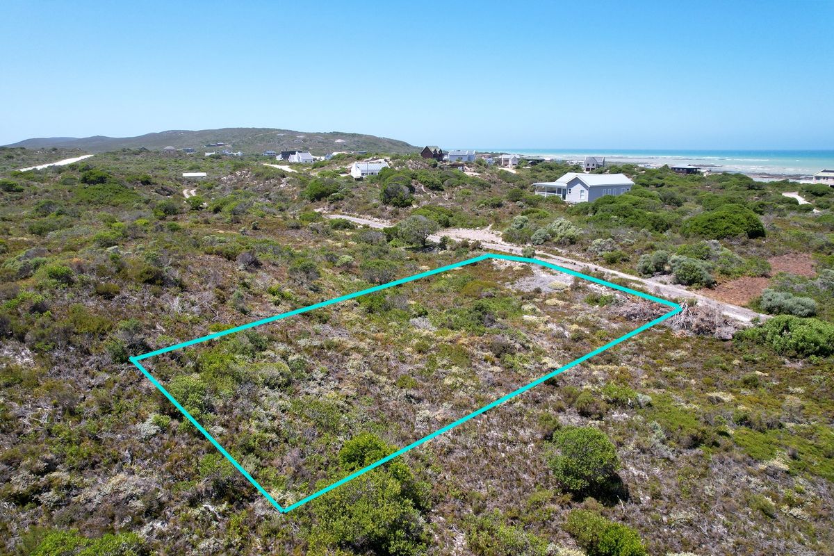 An aerial view of a vacant residential plot featuring natural coastal vegetation, situated in a scenic coastal neighborhood.