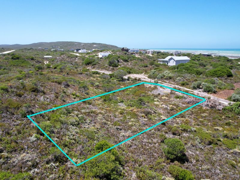 An aerial view of a vacant residential plot featuring natural coastal vegetation, situated in a scenic coastal neighborhood.