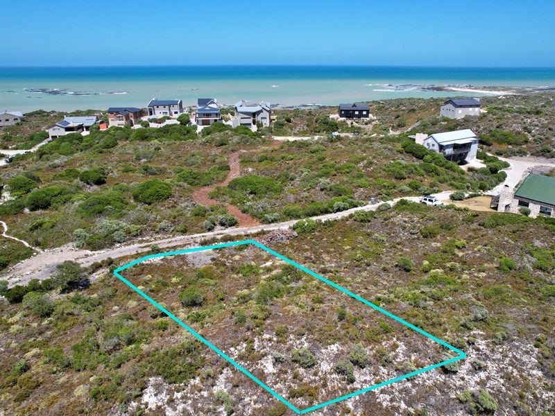 An aerial view of a vacant residential plot featuring natural coastal vegetation and proximity to the ocean.