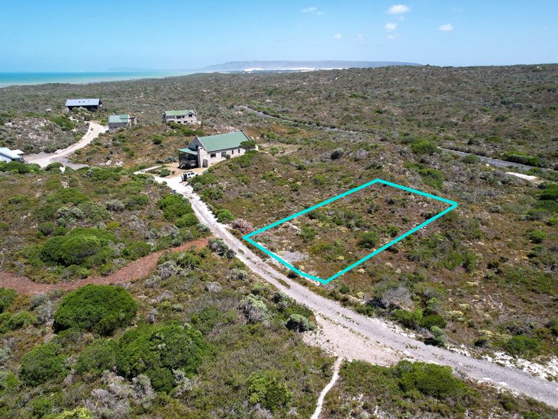 Aerial view of a vacant residential plot featuring natural coastal vegetation and access via a gravel road in a quiet estate setting.