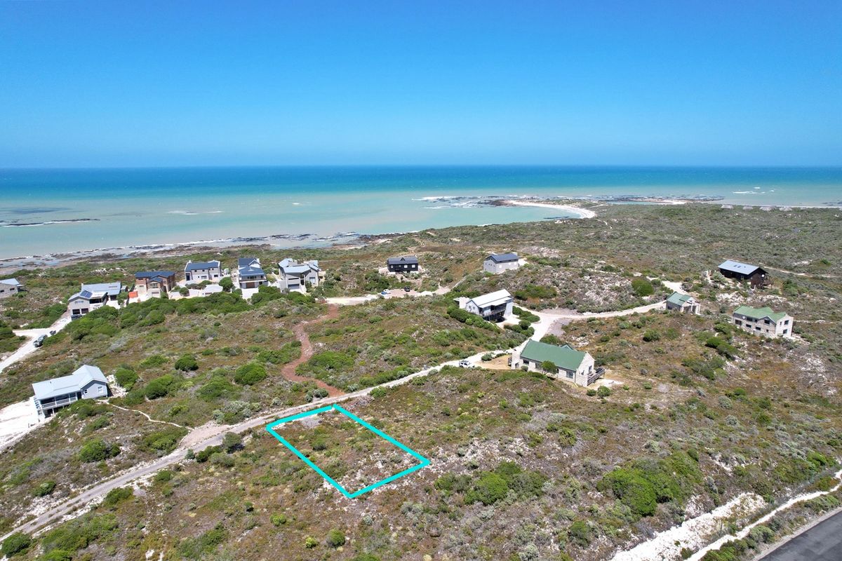 Aerial view of a vacant residential plot situated in a coastal estate, offering proximity to the ocean and surrounding natural vegetation.