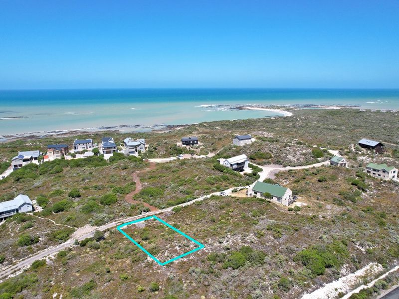 Aerial view of a vacant residential plot situated in a coastal estate, offering proximity to the ocean and surrounding natural vegetation.