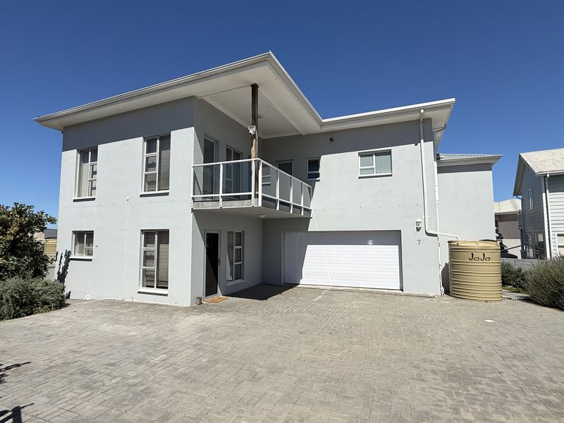 A modern two-story residential property featuring a paved driveway, integrated double garage, upper-level balcony with glass balustrade, and an external water storage tank.