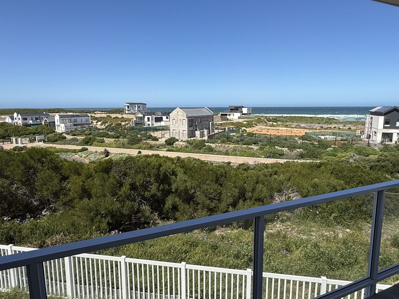 Elevated coastal view overlooking the surrounding estate, natural vegetation, and the ocean horizon from a modern balcony with a glass balustrade.