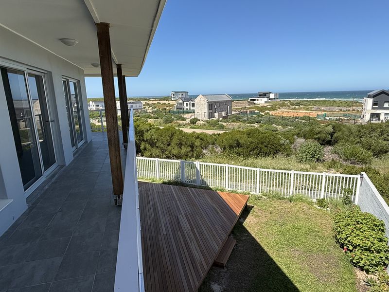 Spacious elevated balcony featuring tiled flooring and wooden supports, overlooking a timber deck, garden area, and coastal landscape views.