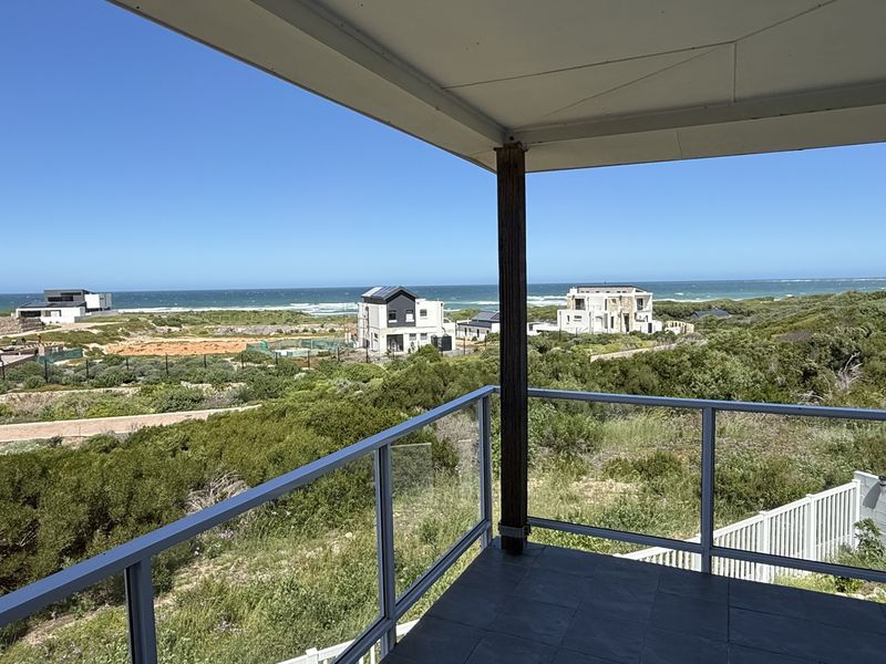 A covered balcony featuring a modern glass balustrade and tiled flooring, offering expansive coastal and landscape views.