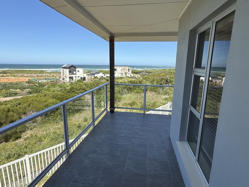 A modern covered balcony featuring tiled flooring and a glass balustrade, offering expansive coastal and ocean views.
