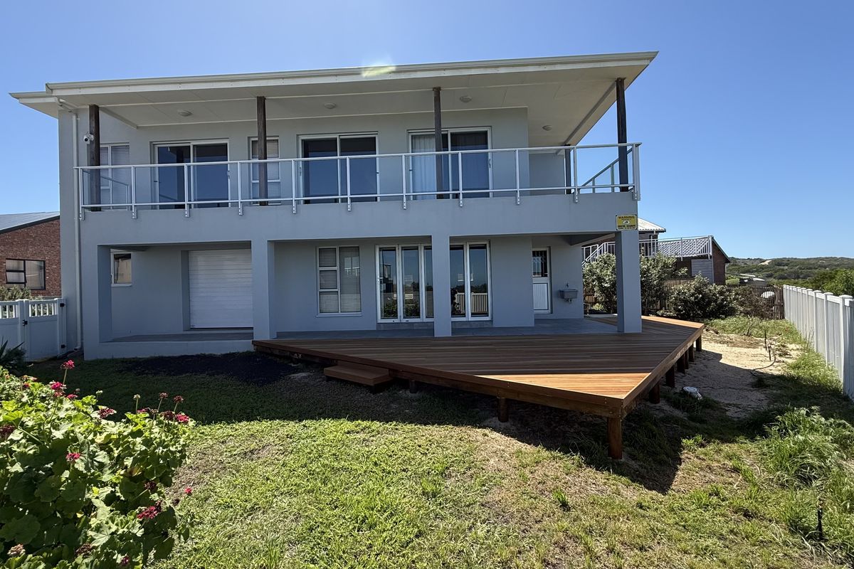 Rear view of a two-story house featuring a large timber deck, upper-level balcony with glass balustrades, and secure sliding door access.