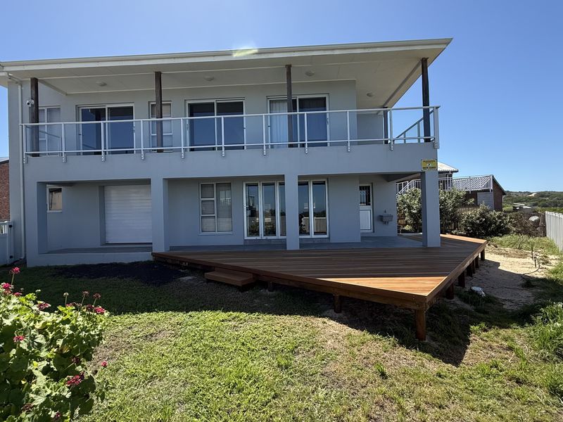 Rear view of a two-story house featuring a large timber deck, upper-level balcony with glass balustrades, and secure sliding door access.