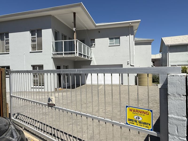Front view of a two-story house featuring a paved driveway, secure sliding gate, attached garage, and an upper-level balcony.