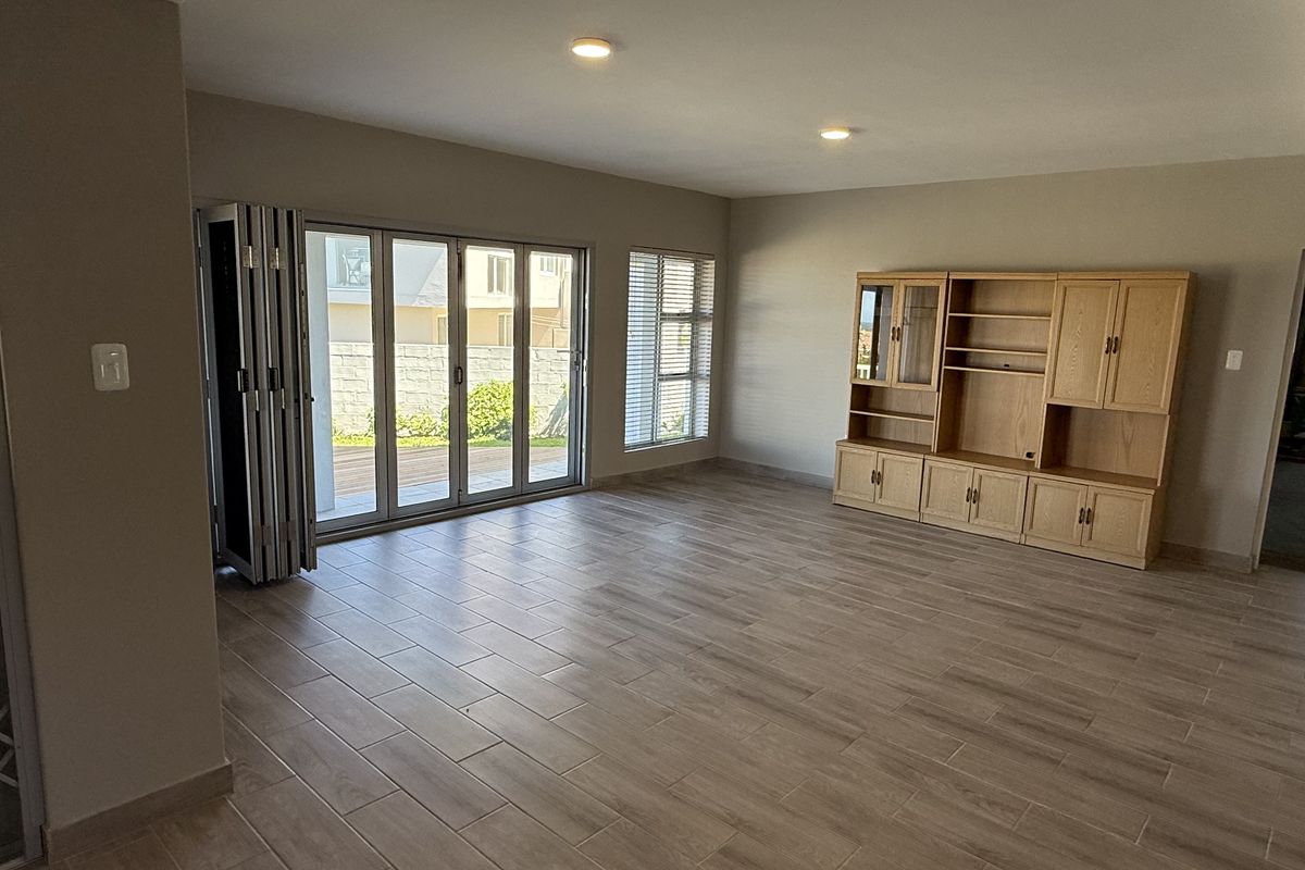 Spacious living room featuring modern wood-look tiled flooring, recessed lighting, and large aluminium stacker doors providing seamless access to the outdoor area.