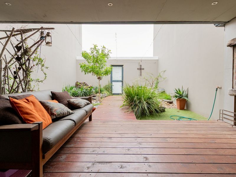 A covered outdoor patio featuring timber decking, a built-in brick fireplace, and direct access to a private courtyard garden area.