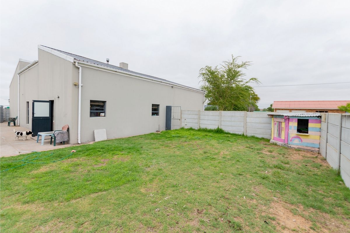 Rear exterior view of the property featuring a paved patio area, a grass lawn, and perimeter precast concrete walling.