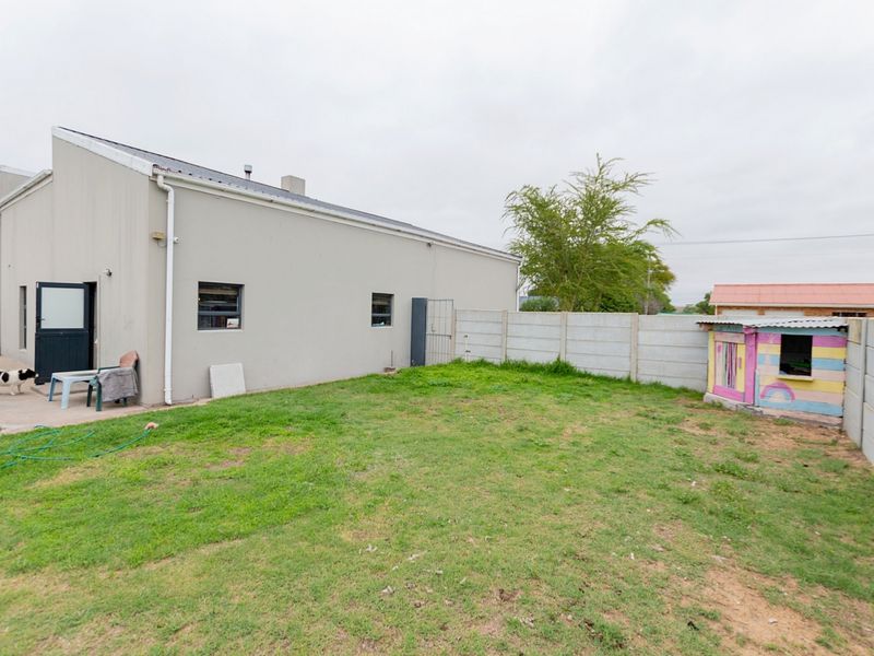 Rear exterior view of the property featuring a paved patio area, a grass lawn, and perimeter precast concrete walling.