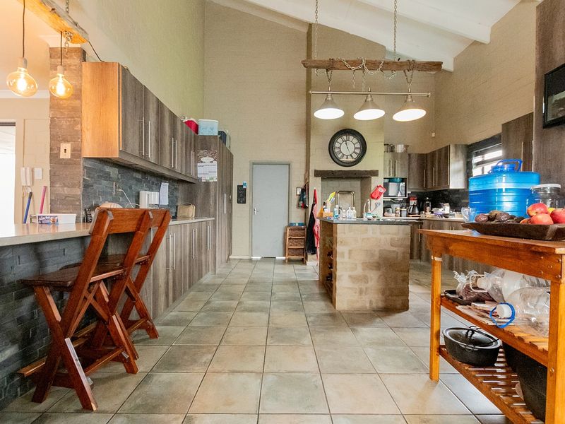 Spacious kitchen featuring vaulted ceilings, extensive built-in cabinetry, a central stone-clad island, and durable tile flooring with a rustic aesthetic.