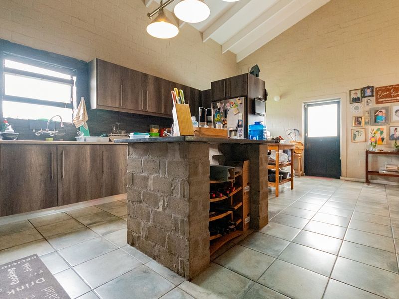 Spacious kitchen featuring dark wood cabinetry, a unique brick-base island, tiled flooring, and high vaulted ceilings with exposed beams.