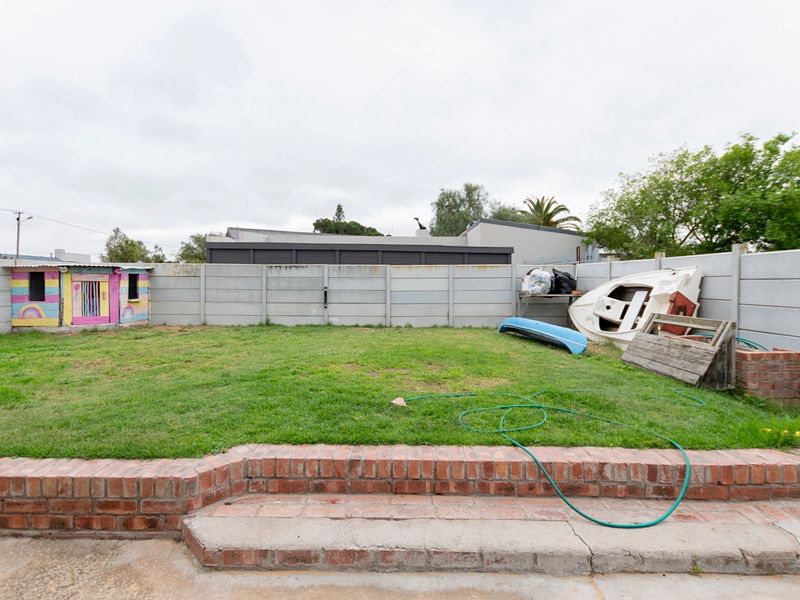 A rear garden area featuring a lawn, brick retaining wall, and concrete boundary fencing, offering potential for landscaping and outdoor improvement.