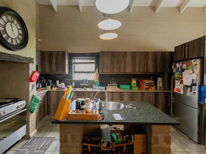A functional kitchen featuring dark wood cabinetry, a central stone-topped island, double sink, and a built-in gas stove under an exposed beam ceiling.