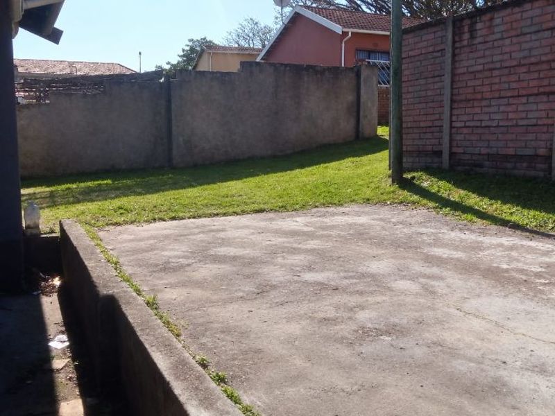 A rear outdoor area featuring a concrete patio, lawn, and perimeter boundary walls.