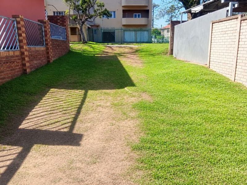 A spacious outdoor garden area featuring brick and concrete boundary walls with metal security fencing, offering potential for landscaping and outdoor improvement.