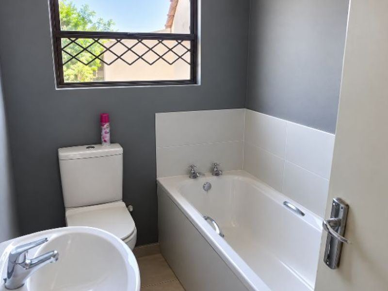 A functional bathroom featuring a bathtub, toilet, and washbasin with modern grey wall finishes and a window with security bars.