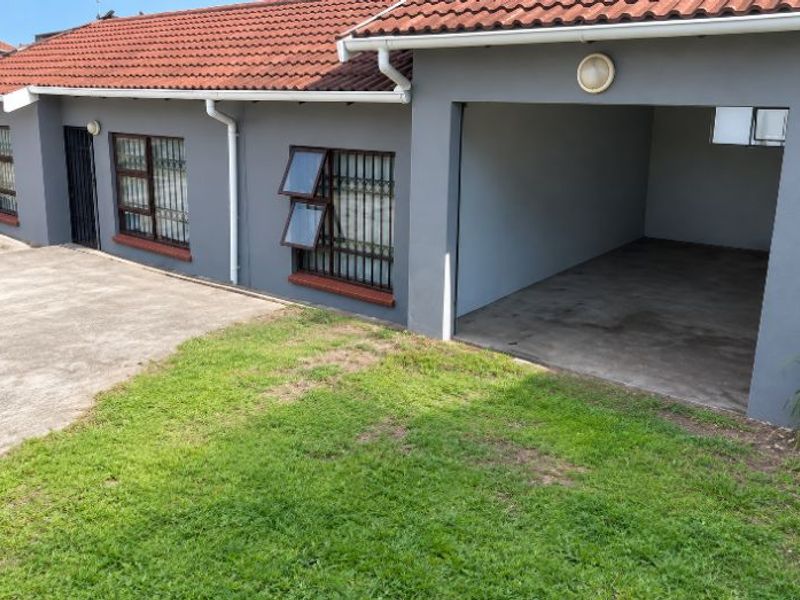 Exterior view of the property featuring a tiled roof, grey facade, security-barred windows, and an integrated garage with a concrete driveway.