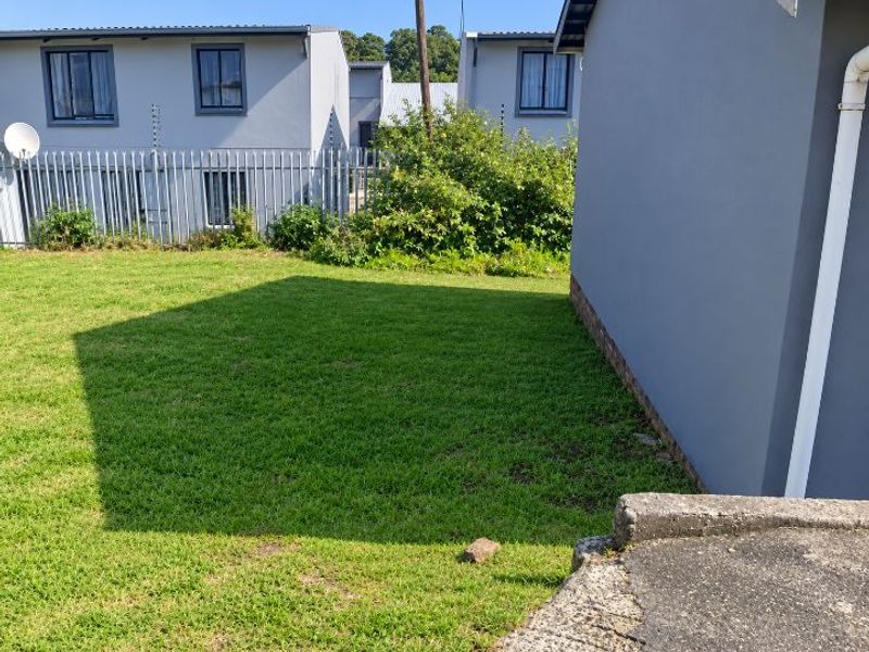 A view of the rear garden area featuring a well-maintained lawn, steel palisade fencing, and a concrete step leading to the building exterior.