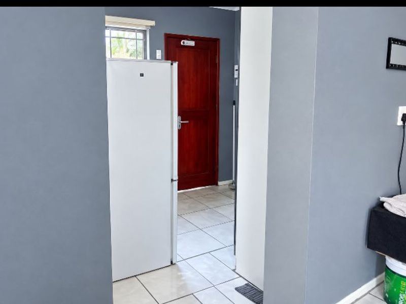A functional scullery or utility area featuring tiled flooring, a solid timber door, and a window with security bars.