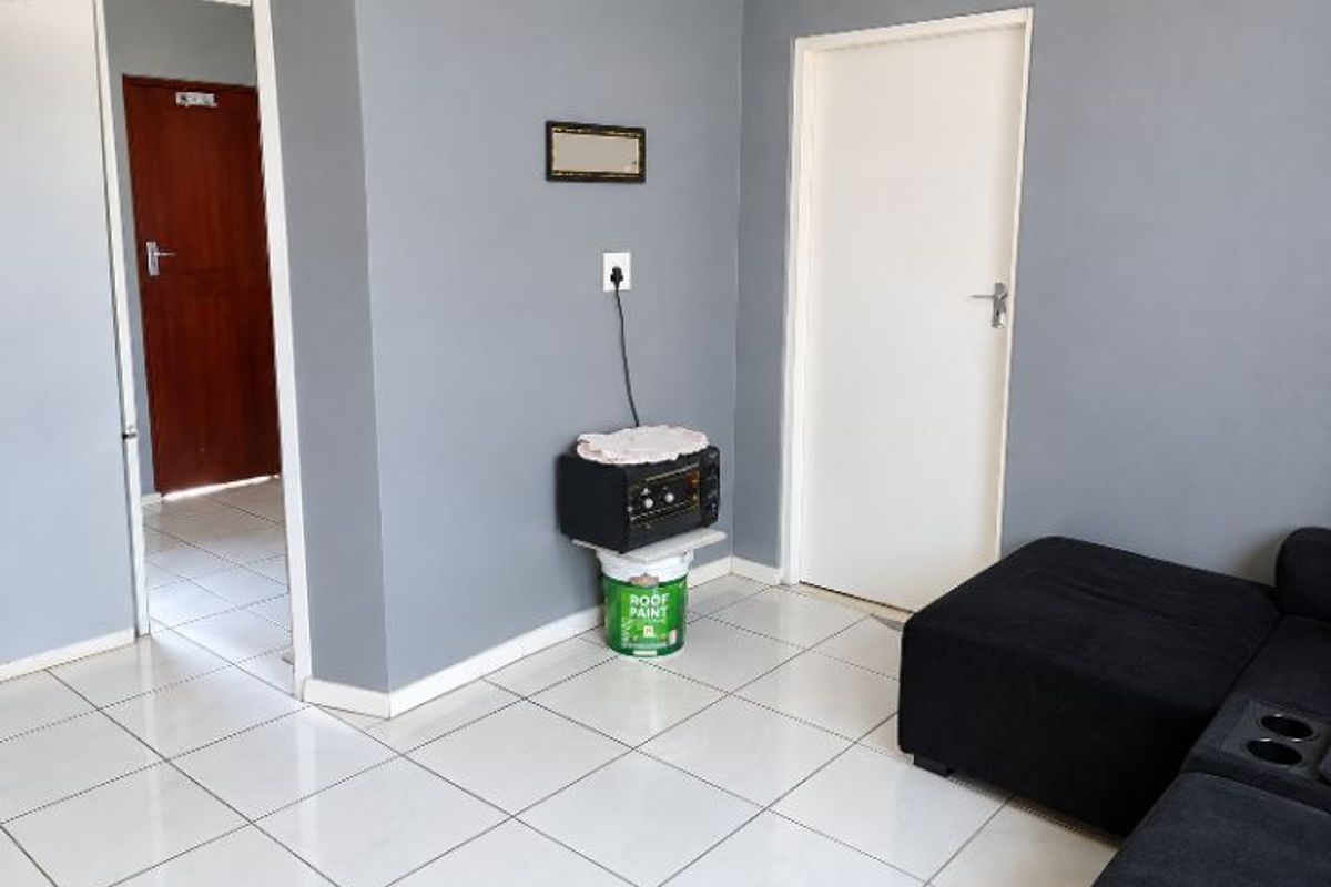 A living area featuring neutral grey walls and white tiled flooring, providing a clean and functional space with access to adjacent rooms.