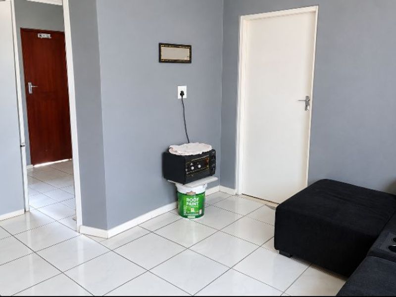 A living area featuring neutral grey walls and white tiled flooring, providing a clean and functional space with access to adjacent rooms.