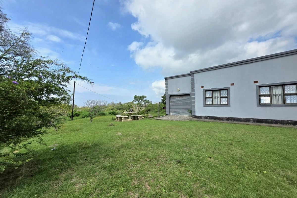 Rear view of the property featuring a lawn, garage access, and windows with security bars.