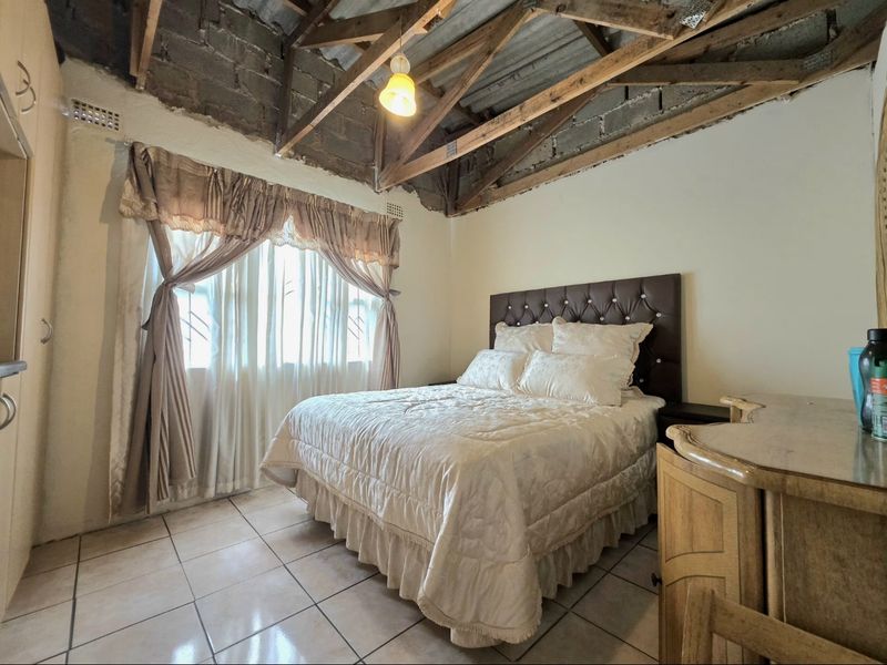 A bedroom featuring tiled flooring, built-in cabinetry, and an unfinished ceiling with exposed timber roof trusses and concrete blockwork.