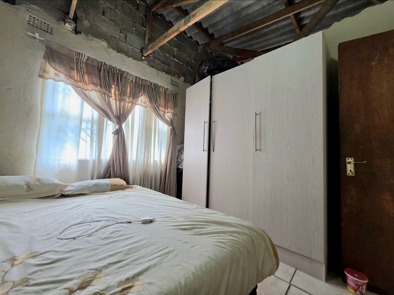A bedroom featuring a built-in wardrobe, tiled flooring, and exposed roof trusses with unfinished brick walls.