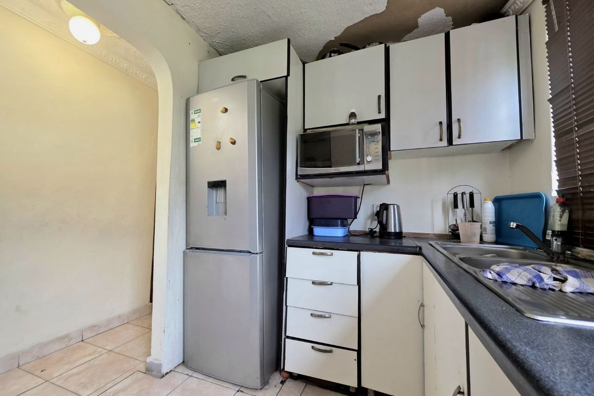 Compact kitchen featuring built-in cabinetry, laminate countertops, and a stainless steel sink, currently requiring ceiling repairs and cosmetic updates.