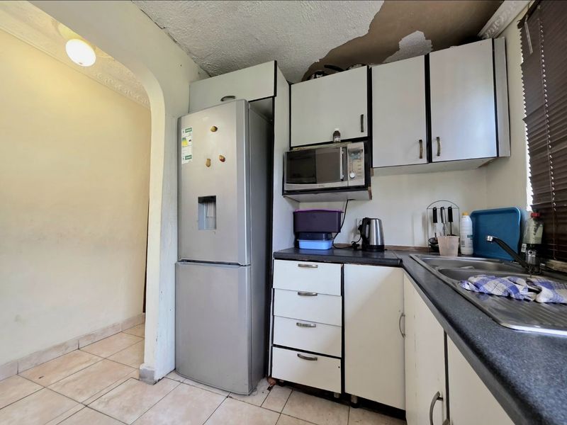 Compact kitchen featuring built-in cabinetry, laminate countertops, and a stainless steel sink, currently requiring ceiling repairs and cosmetic updates.