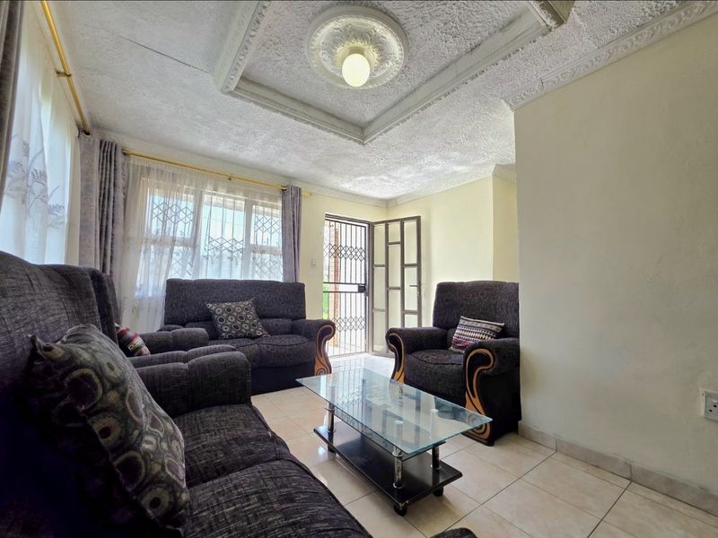 A living room featuring tiled flooring, a decorative ceiling rose with coved cornicing, and a security gate leading to the exterior.