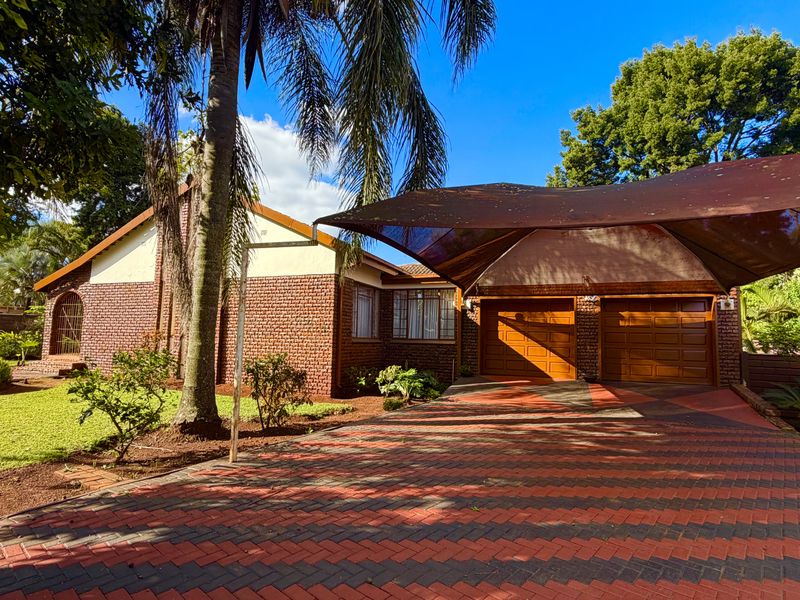 Front exterior view of a brick house featuring a double garage, paved driveway, and a large shade sail structure.