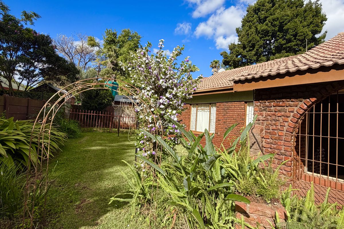 A view of the rear garden featuring a brick facade, tiled roof, and established landscaping with a decorative metal garden arch.