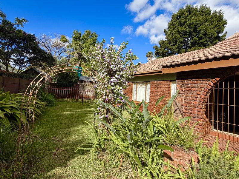 A view of the rear garden featuring a brick facade, tiled roof, and established landscaping with a decorative metal garden arch.