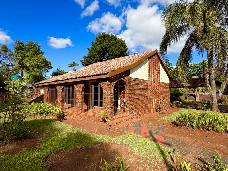 A charming face brick house featuring a tiled roof, arched patio design with security bars, and a well-maintained garden with a paved walkway.