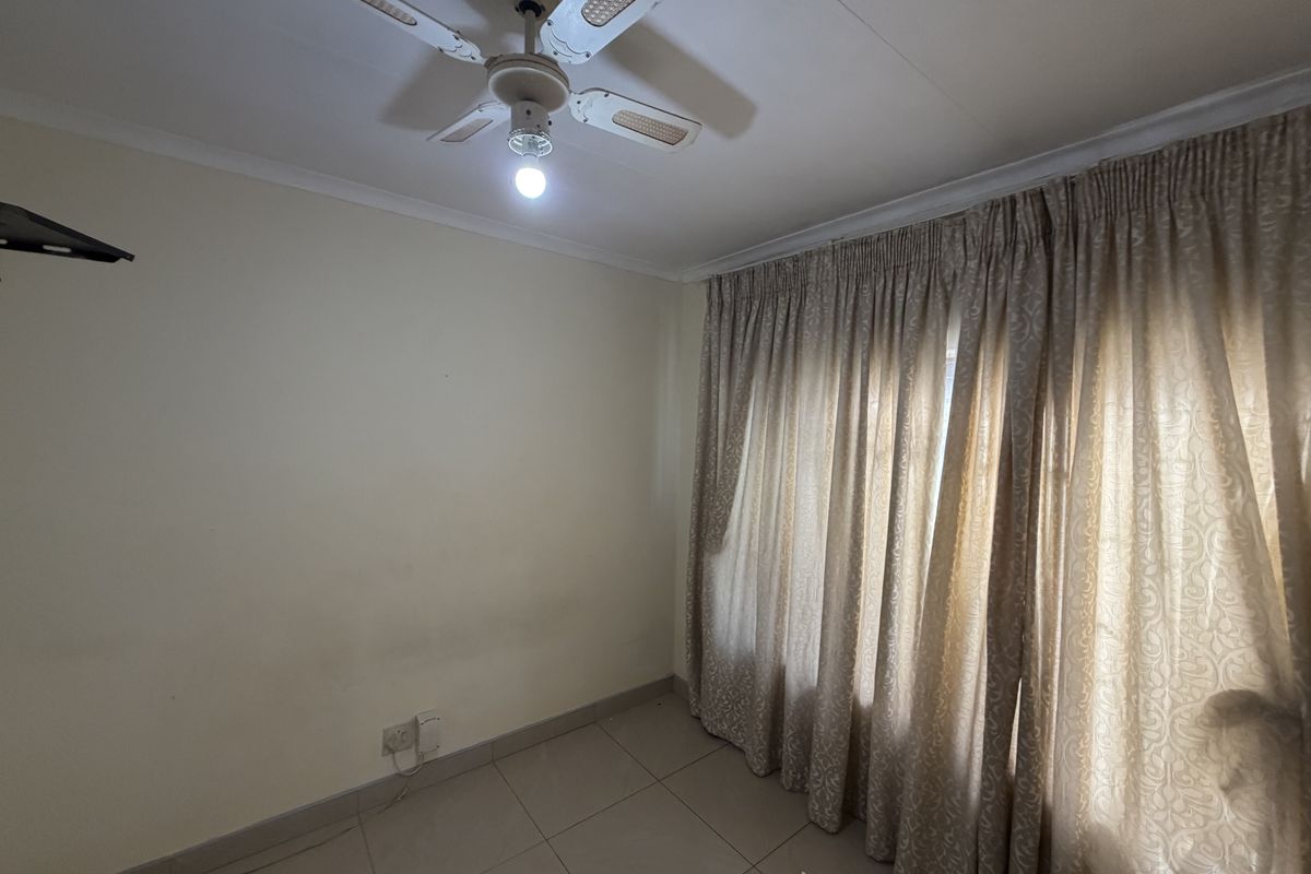 A vacant bedroom featuring tiled flooring, a ceiling fan, and full-length curtain tracks, offering a neutral canvas for personalization.
