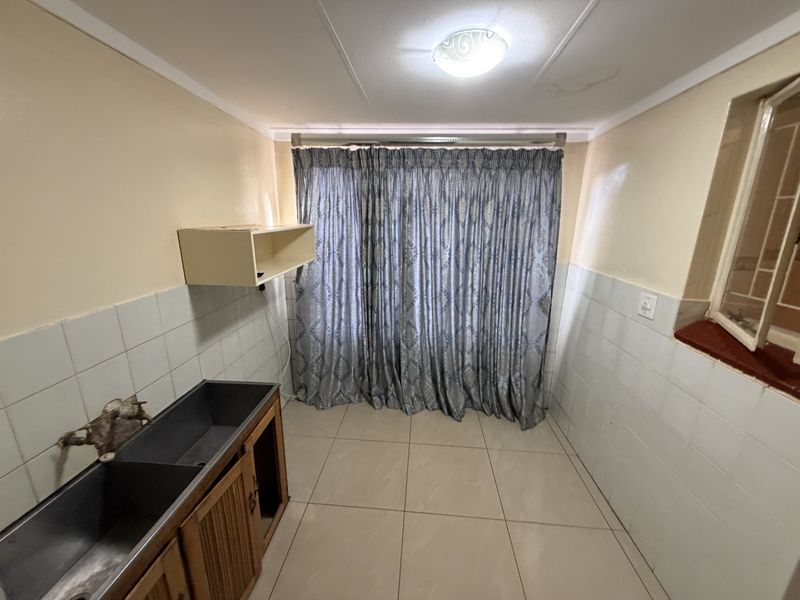 A functional laundry room featuring tiled flooring, a double basin sink with built-in cabinetry, and tiled wall splashbacks.