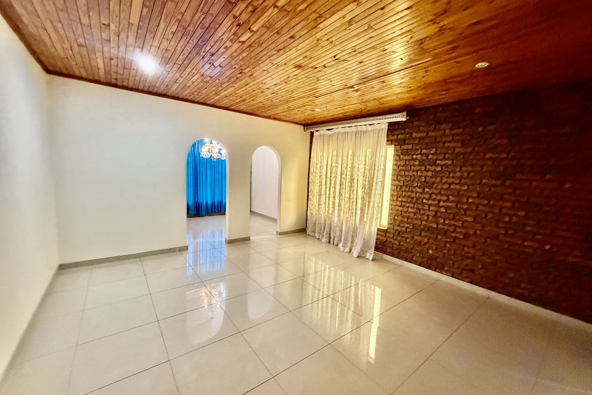 Spacious living area featuring a warm timber ceiling, an exposed brick feature wall, and polished porcelain floor tiles with elegant arched entryways.