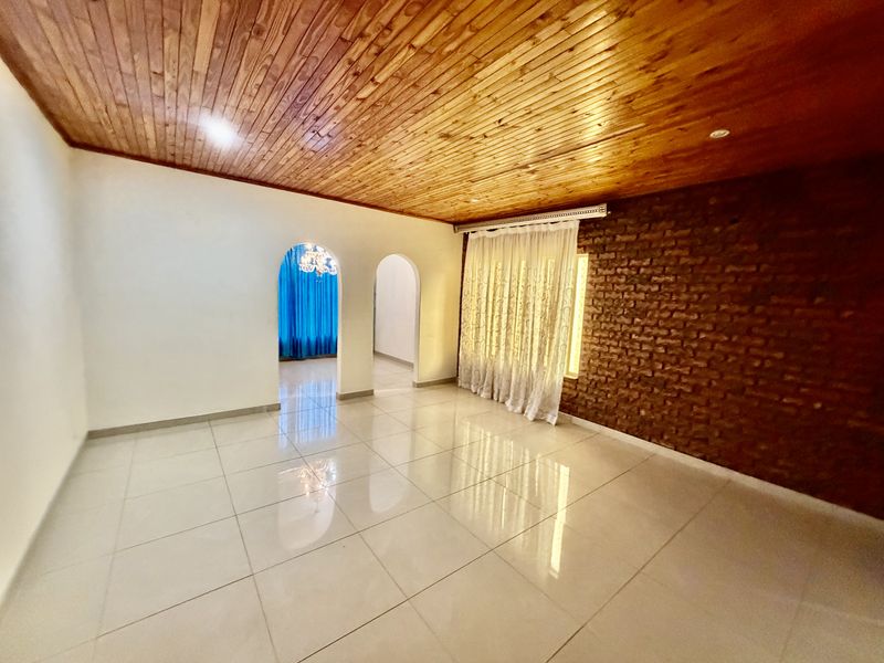 Spacious living area featuring a warm timber ceiling, an exposed brick feature wall, and polished porcelain floor tiles with elegant arched entryways.