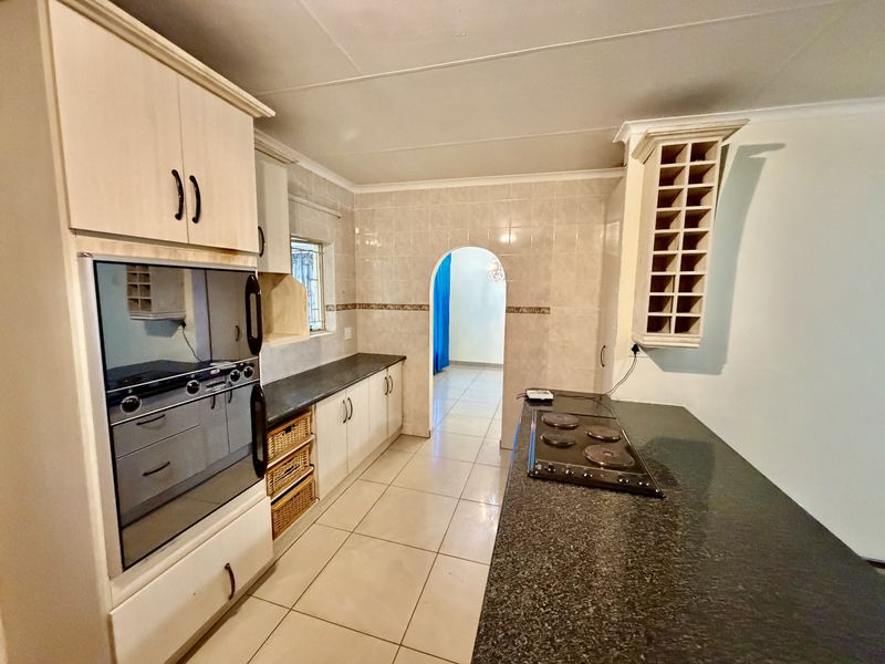 A functional kitchen featuring granite countertops, built-in oven, electric hob, tiled flooring, and a decorative archway leading to the adjacent living space.