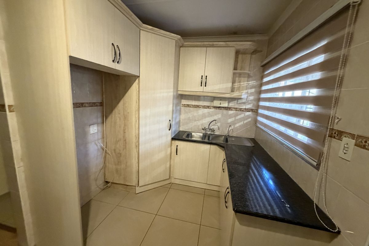 A functional kitchen featuring built-in cabinetry, granite countertops, a double basin sink, and tiled flooring with neutral finishes.
