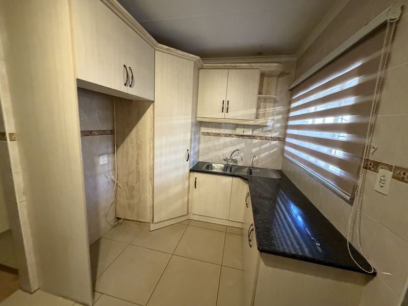 A functional kitchen featuring built-in cabinetry, granite countertops, a double basin sink, and tiled flooring with neutral finishes.