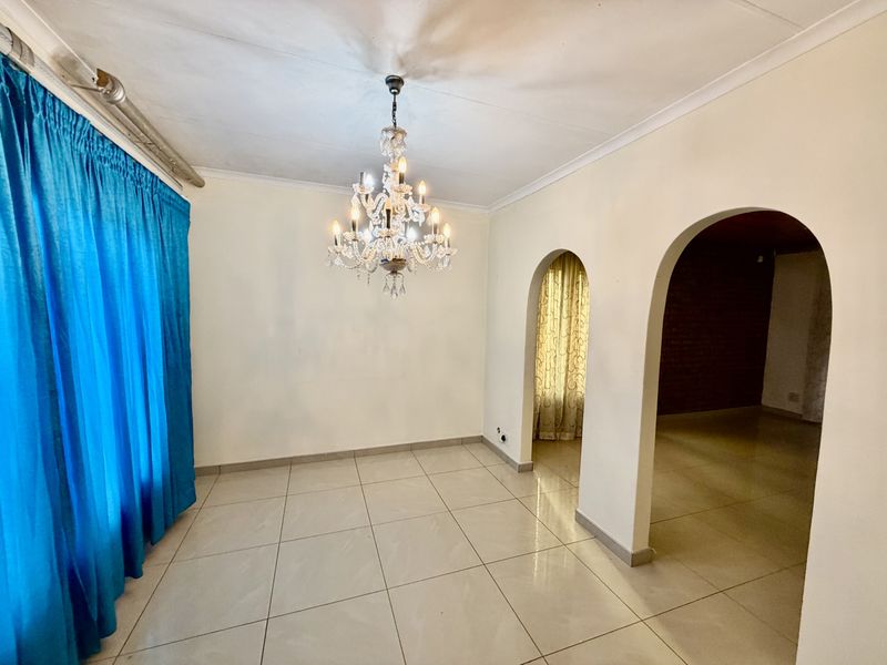 An empty living area featuring tiled flooring, arched architectural doorways, and a decorative crystal chandelier, showing signs of ceiling wear.
